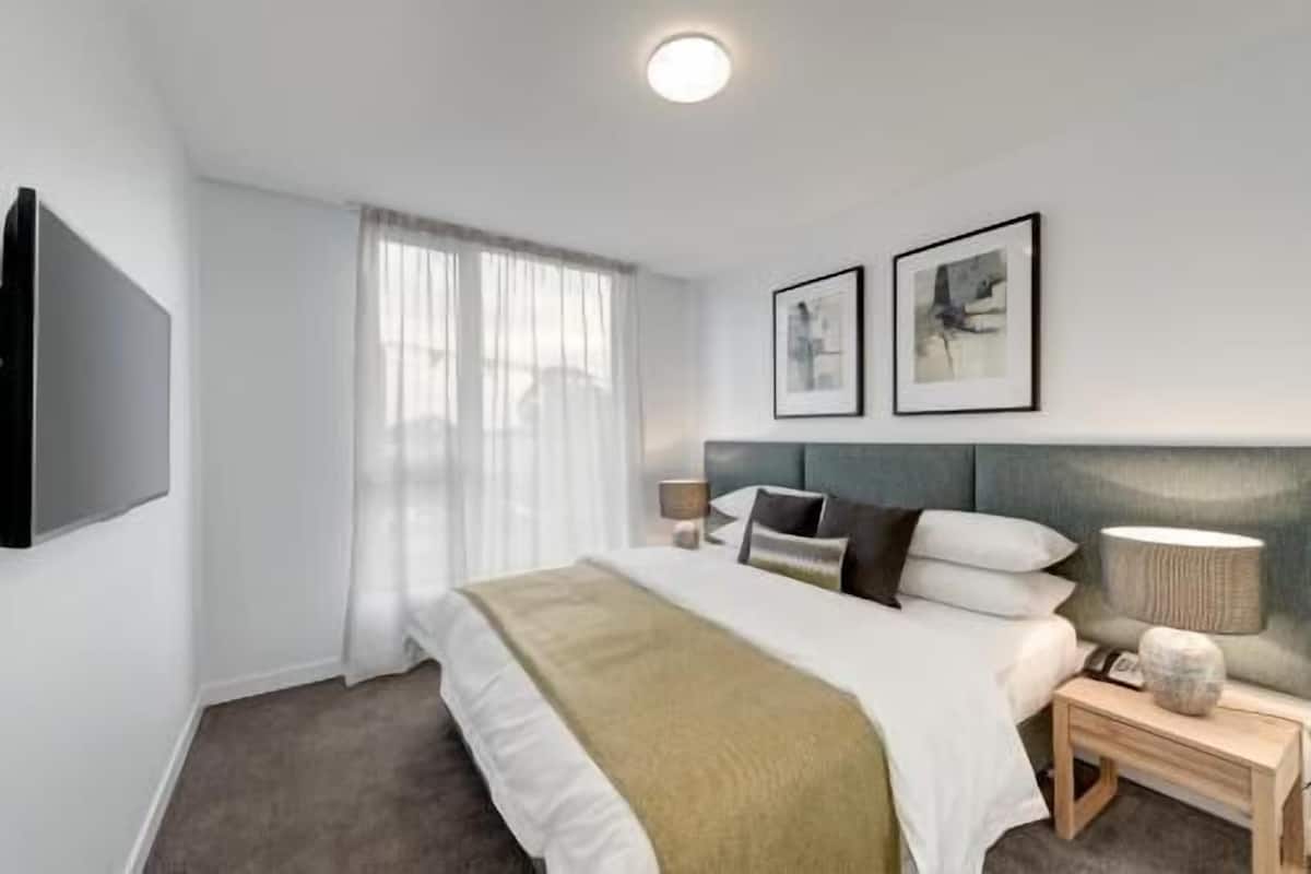 Habitación de hotel moderna con una cama grande, un televisor de pantalla plana, dos cuadros en la pared y una lámpara de noche.