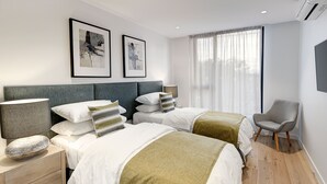 A modern hotel room with two beds, a desk, a chair, and a large window with curtains. - Camberwell Serviced Apartment Hotel (Hawthorn East)