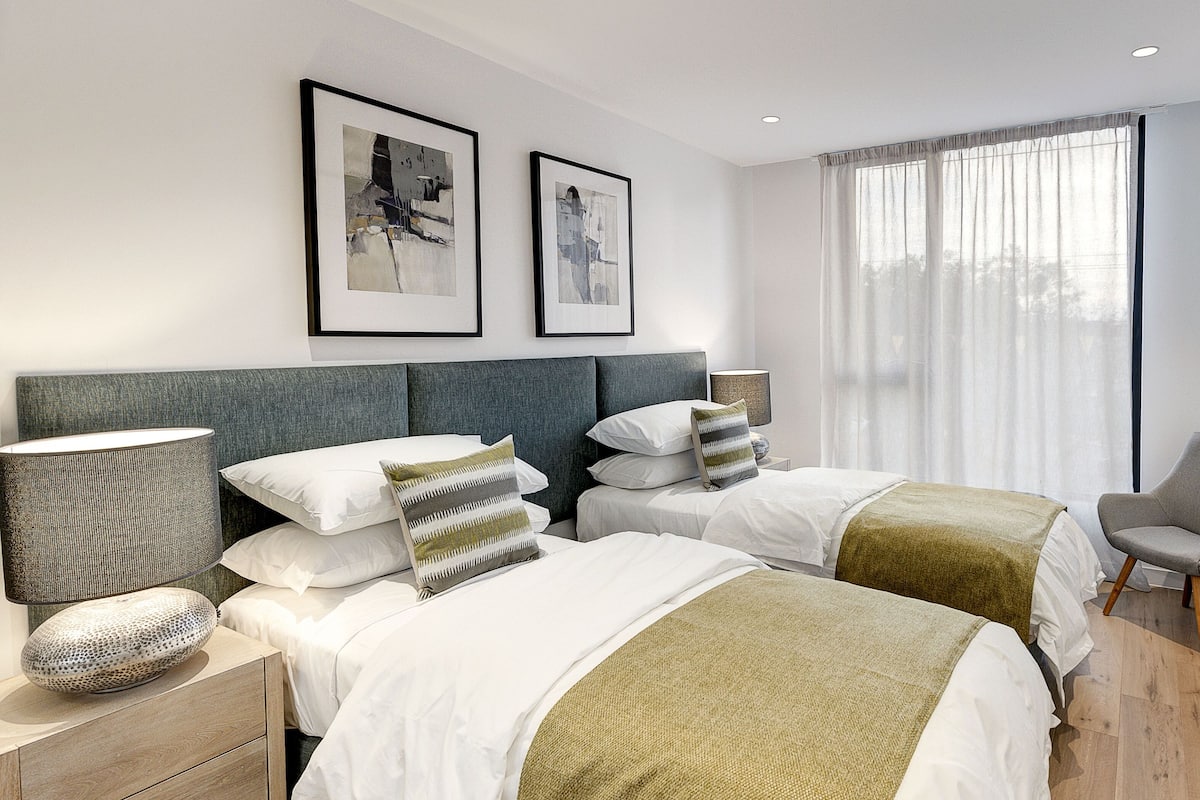 Una habitación de hotel moderna con dos camas, un escritorio, una silla y un ventanal con cortinas.