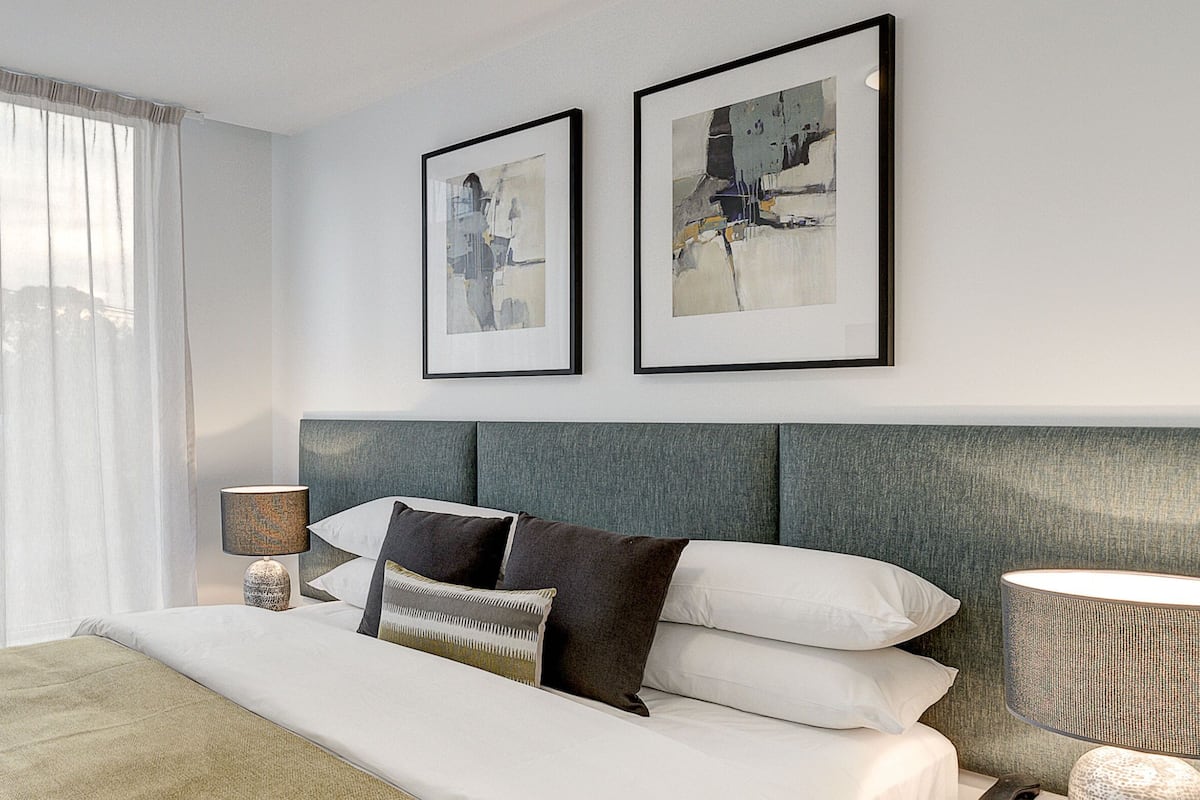 Una habitación de hotel con una cama, una mesita de noche, una lámpara y dos cuadros en la pared.