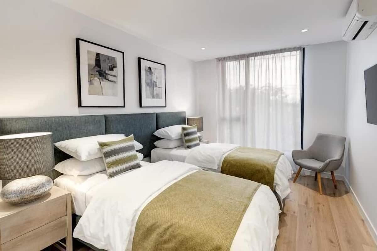 Una habitación de hotel moderna con dos camas, un escritorio, una silla, un televisor y obras de arte en la pared.