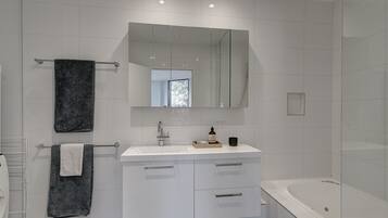 Uma casa de banho moderna com máquina de lavar, lavatório com espelho e banheira.