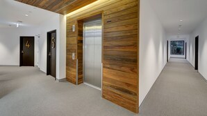 A modern hallway with wooden paneling, numbered doors, and an elevator. - Camberwell Serviced Apartment Hotel (Hawthorn East)