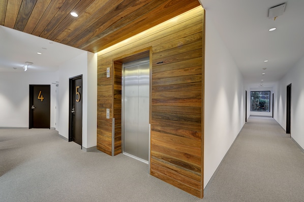 Un couloir moderne avec des lambris en bois, des portes numérotées et un ascenseur.
