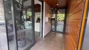A hallway with glass doors leading to a reception area, a potted plant, and a wooden wall. - Camberwell Serviced Apartment Hotel (Hawthorn East)