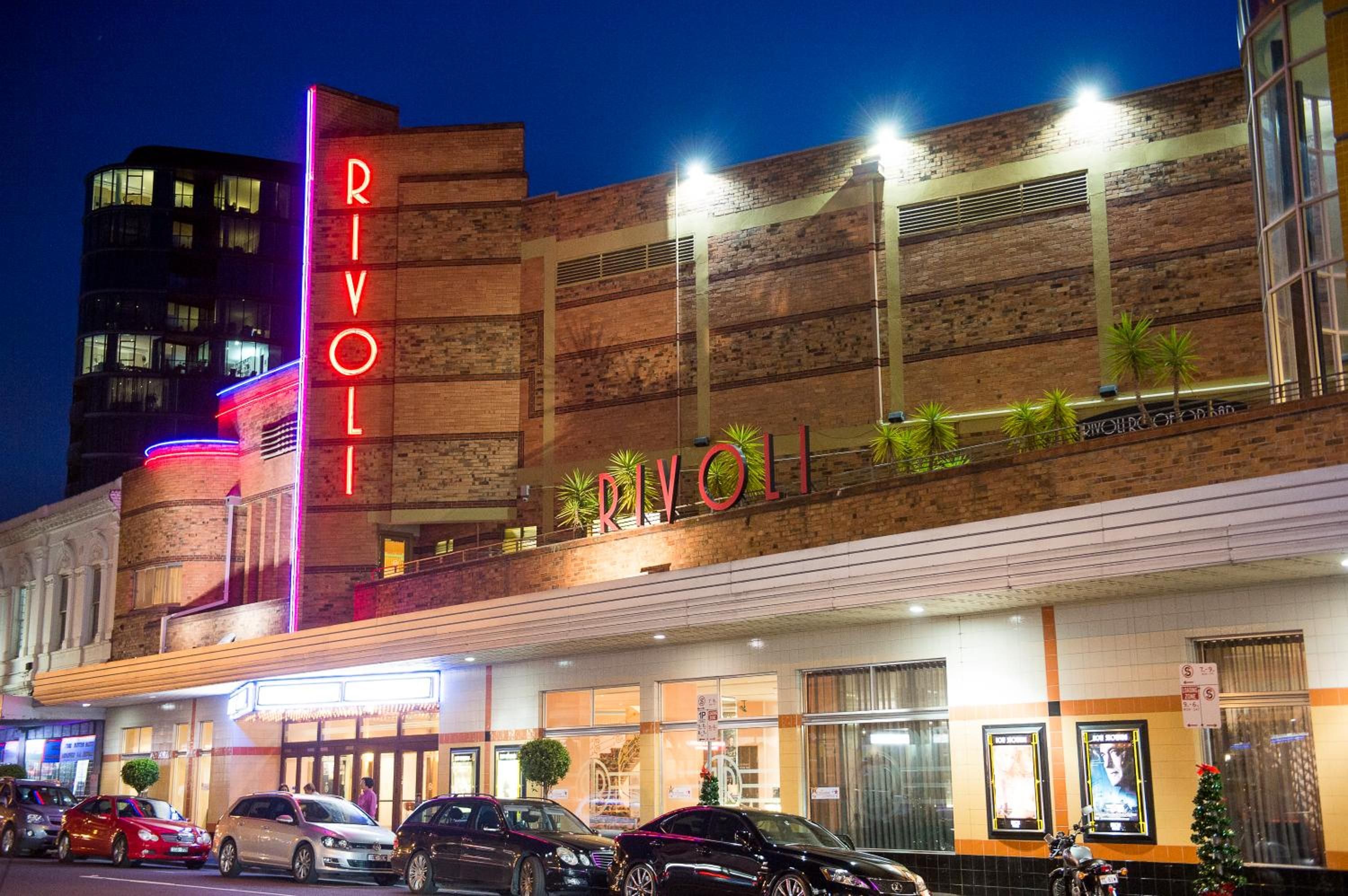 Un edificio con un llamativo letrero 'RIVOLI', varias ventanas y un estacionamiento con coches.