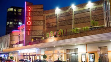 Un edificio con un llamativo letrero 'RIVOLI', varias ventanas y un estacionamiento con coches.