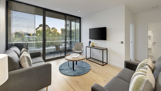 A modern living room with a sofa, a coffee table, and a TV mounted on the wall. - Camberwell Serviced Apartment Hotel (Hawthorn East)