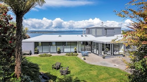 Ein modernes Haus mit einem großen Wintergarten, einem gepflegten Rasen und Meerblick.