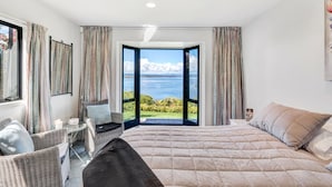 Ein Schlafzimmer mit einem großen Bett, einer Sitzecke mit Tisch und Blick auf das Meer durch eine offene Tür.