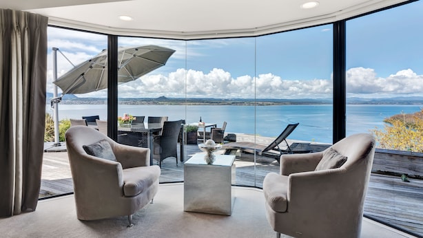 Ein modernes Wohnzimmer mit einer großen Glaswand, die einen weiten Blick auf das Meer und die Wolken bietet.