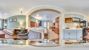 A panoramic view of a hotel room with a living area, bedroom, and kitchenette.
