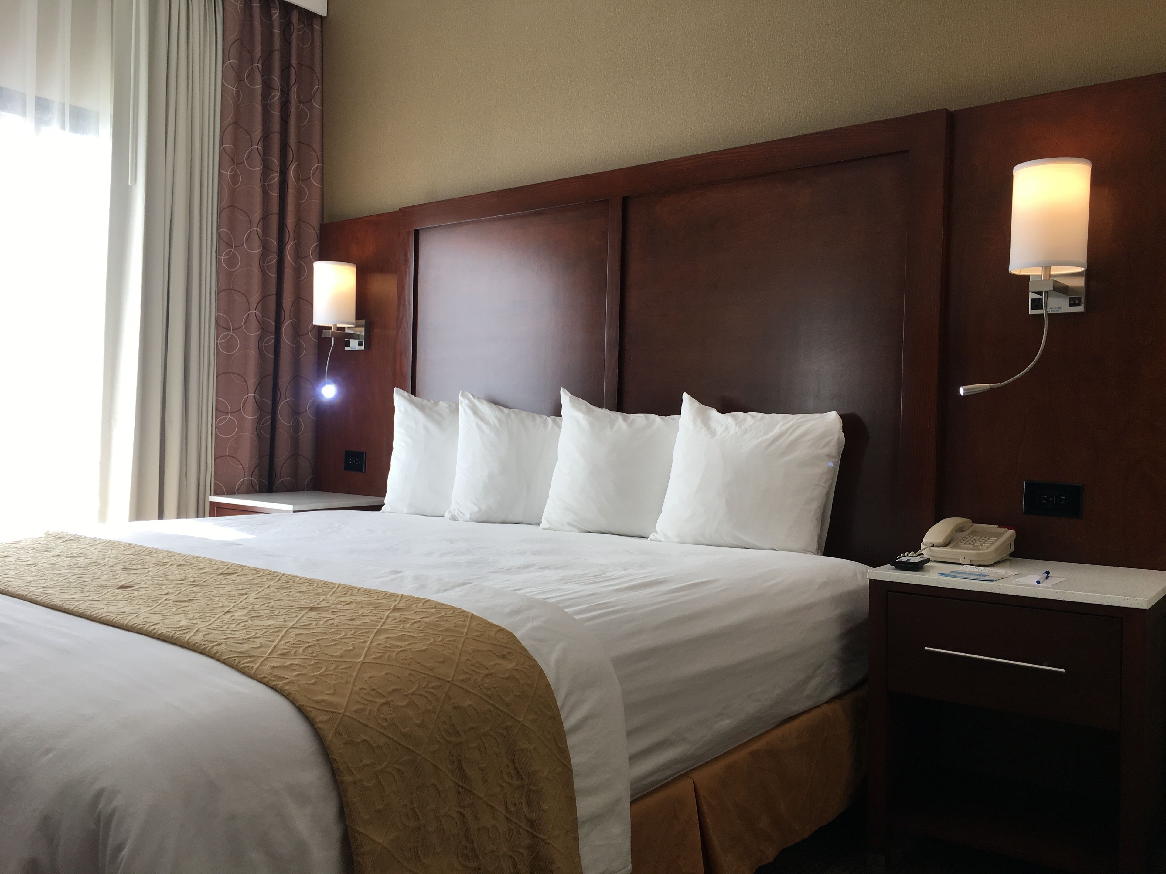 A hotel room with a large bed, two bedside lamps, a nightstand with a phone, and a window with curtains.