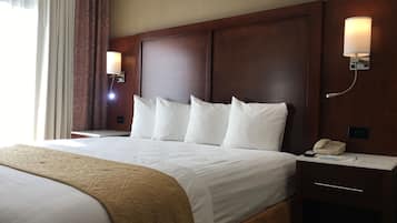A hotel room with a large bed, two bedside lamps, a nightstand with a phone, and a window with curtains.
