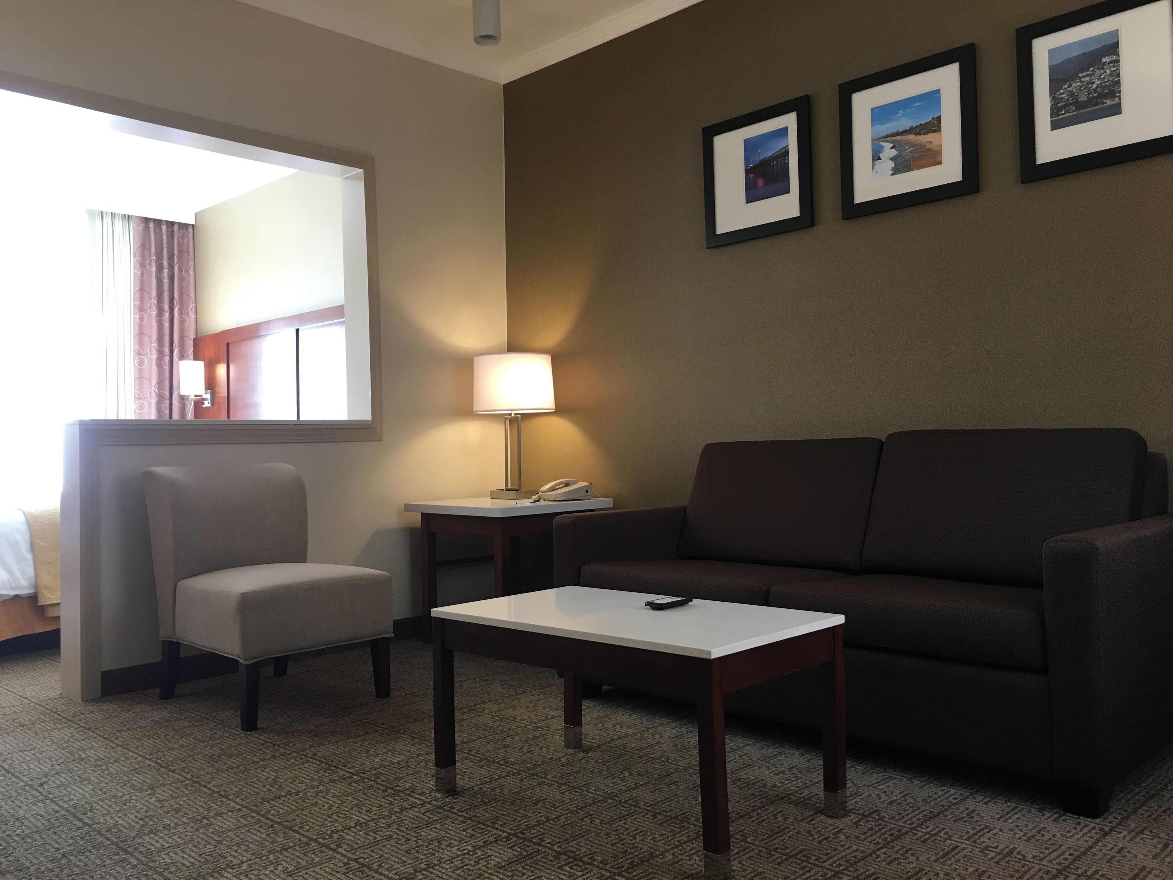 Une chambre d’hôtel avec un canapé, un fauteuil, une petite table, une lampe et trois tableaux encadrés au mur.