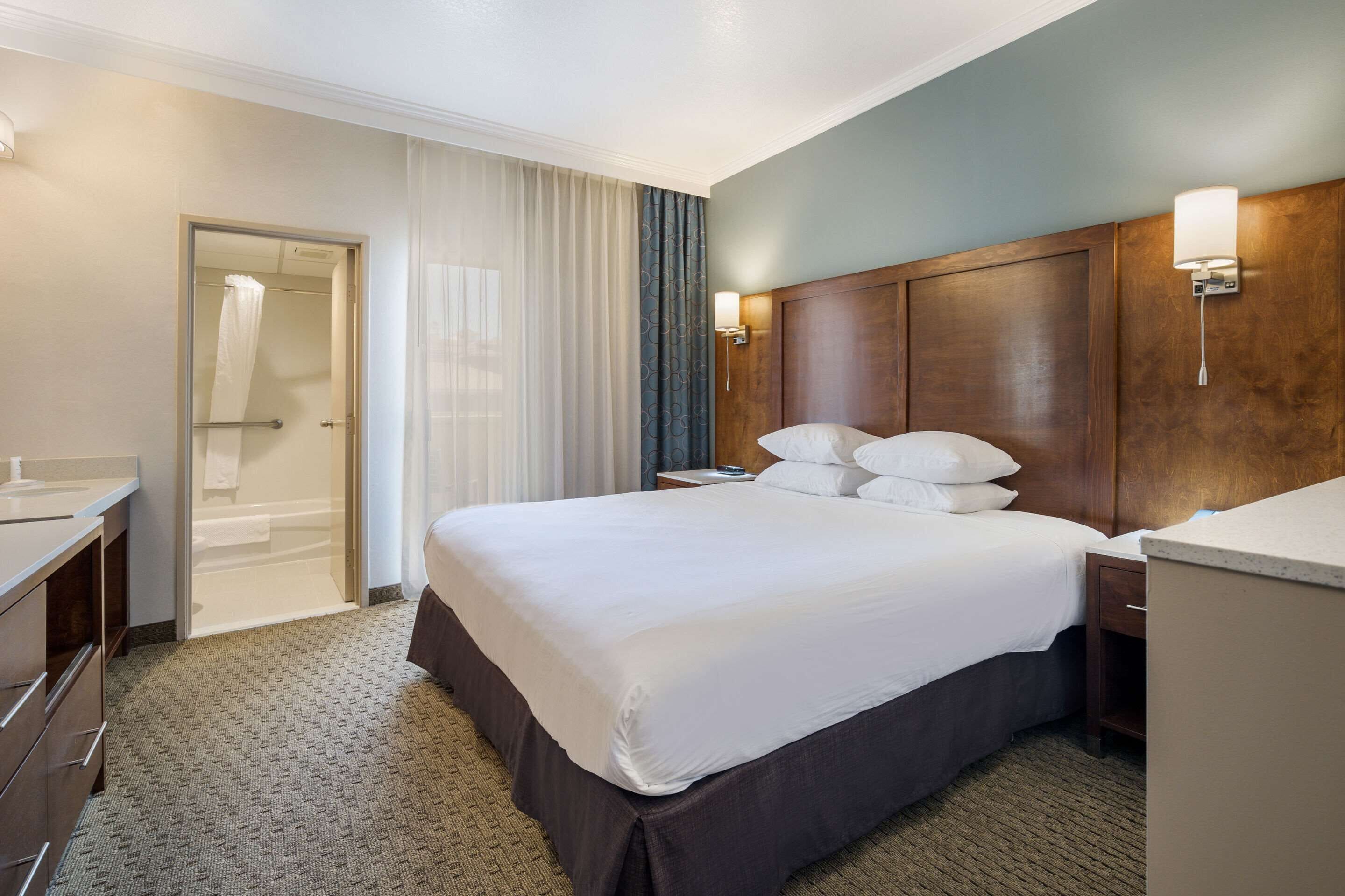 Ein Hotelzimmer mit einem großen Bett, einem Holz-Kopfteil, einem Nachttisch und einem Badezimmer mit Dusche und Toilette.
