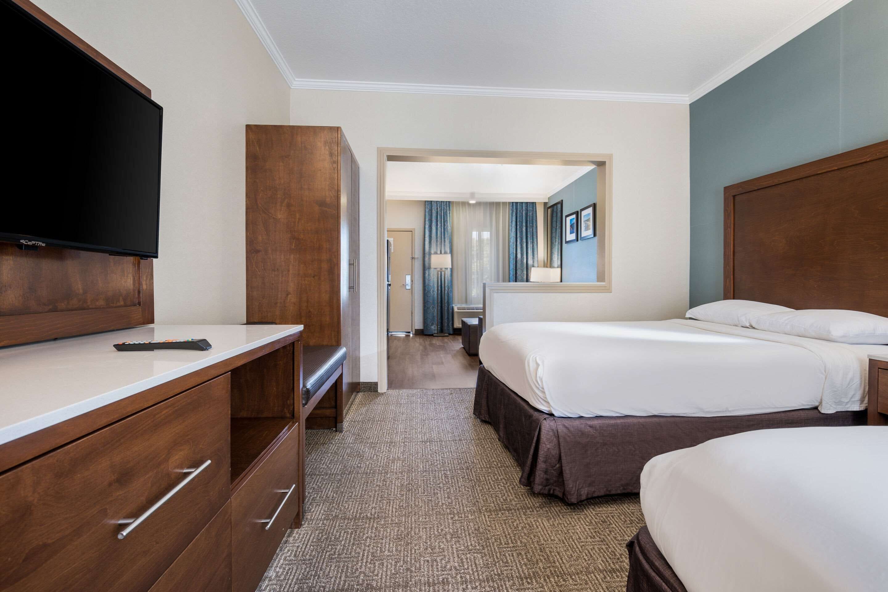 Une chambre d’hôtel équipée d’une télévision à écran plat, d’un bureau avec des tiroirs, de deux lits et d’une salle de bain visible par une porte.