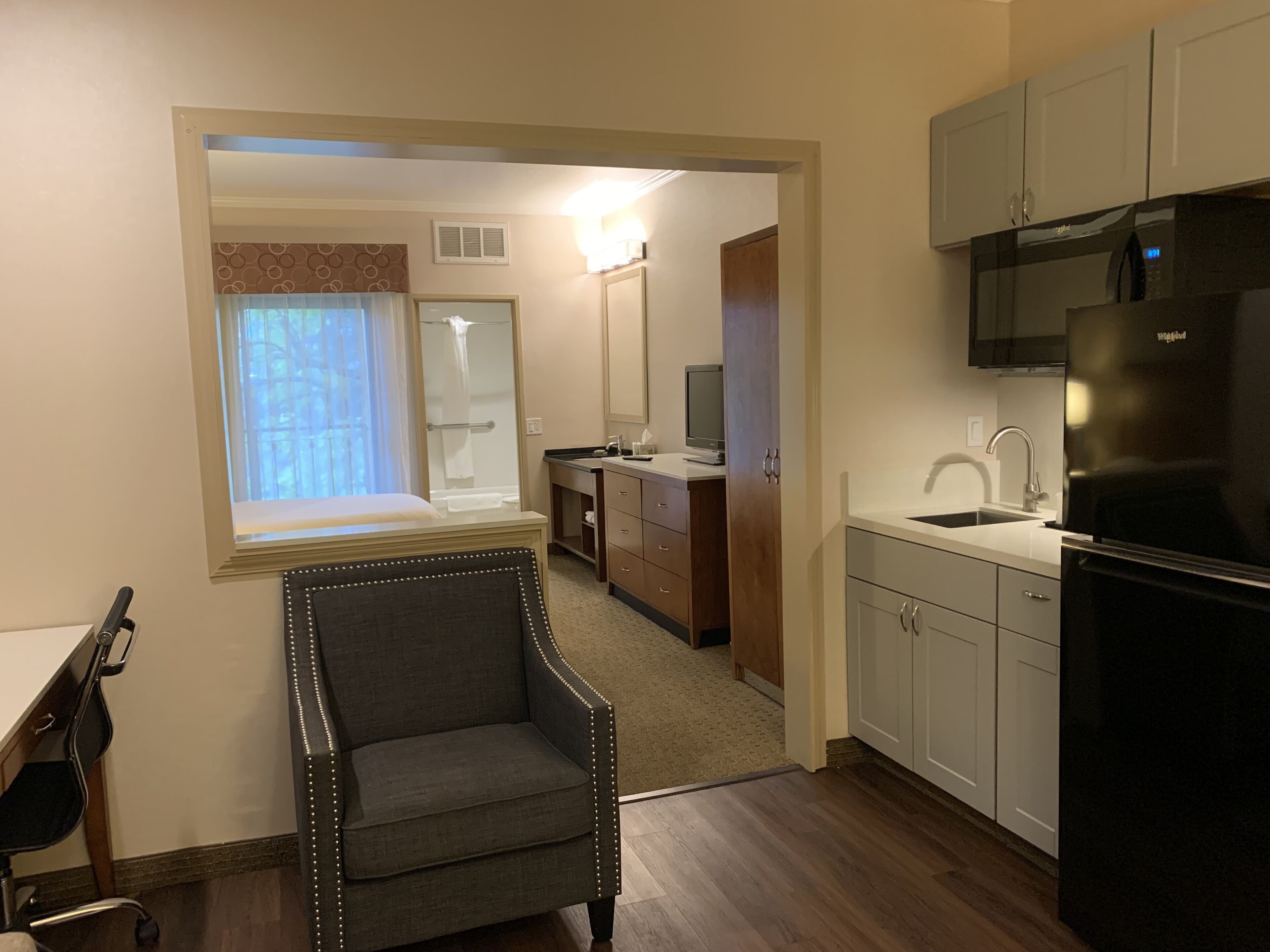 Una habitación de hotel compacta con kitchenette, zona de estar, ducha y un espejo grande.
