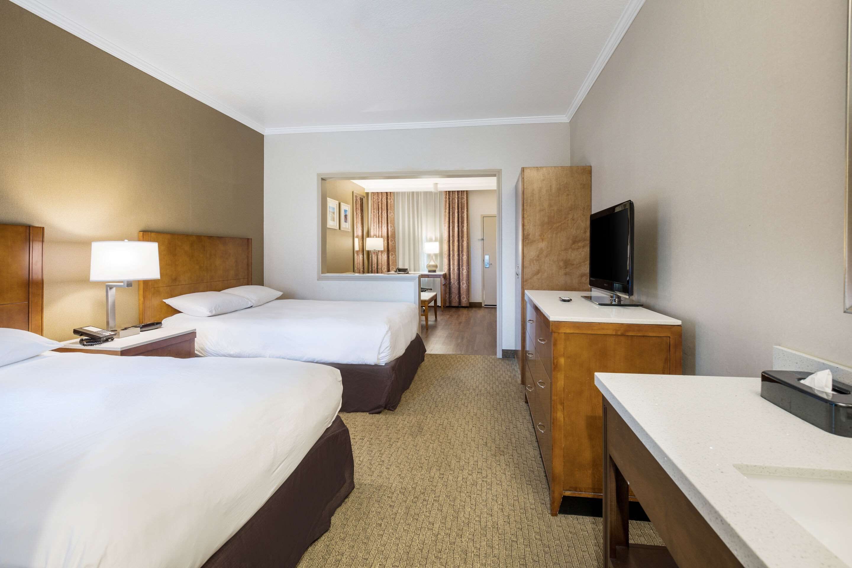 Habitación de hotel con dos camas, un escritorio, un televisor y un espejo.