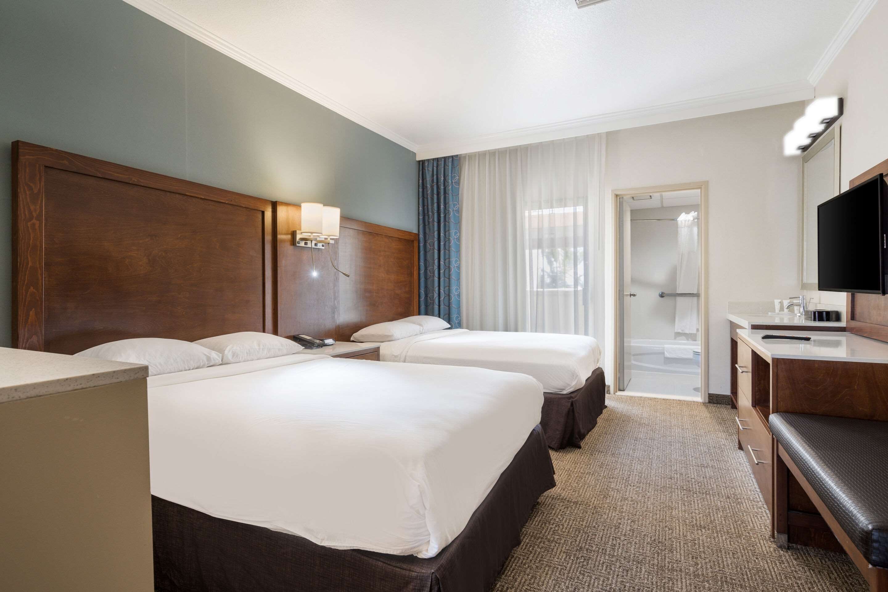 Ein Hotelzimmer mit zwei Betten, einem Schreibtisch mit Fernseher, einem Badezimmer mit Dusche und Blick nach draußen.