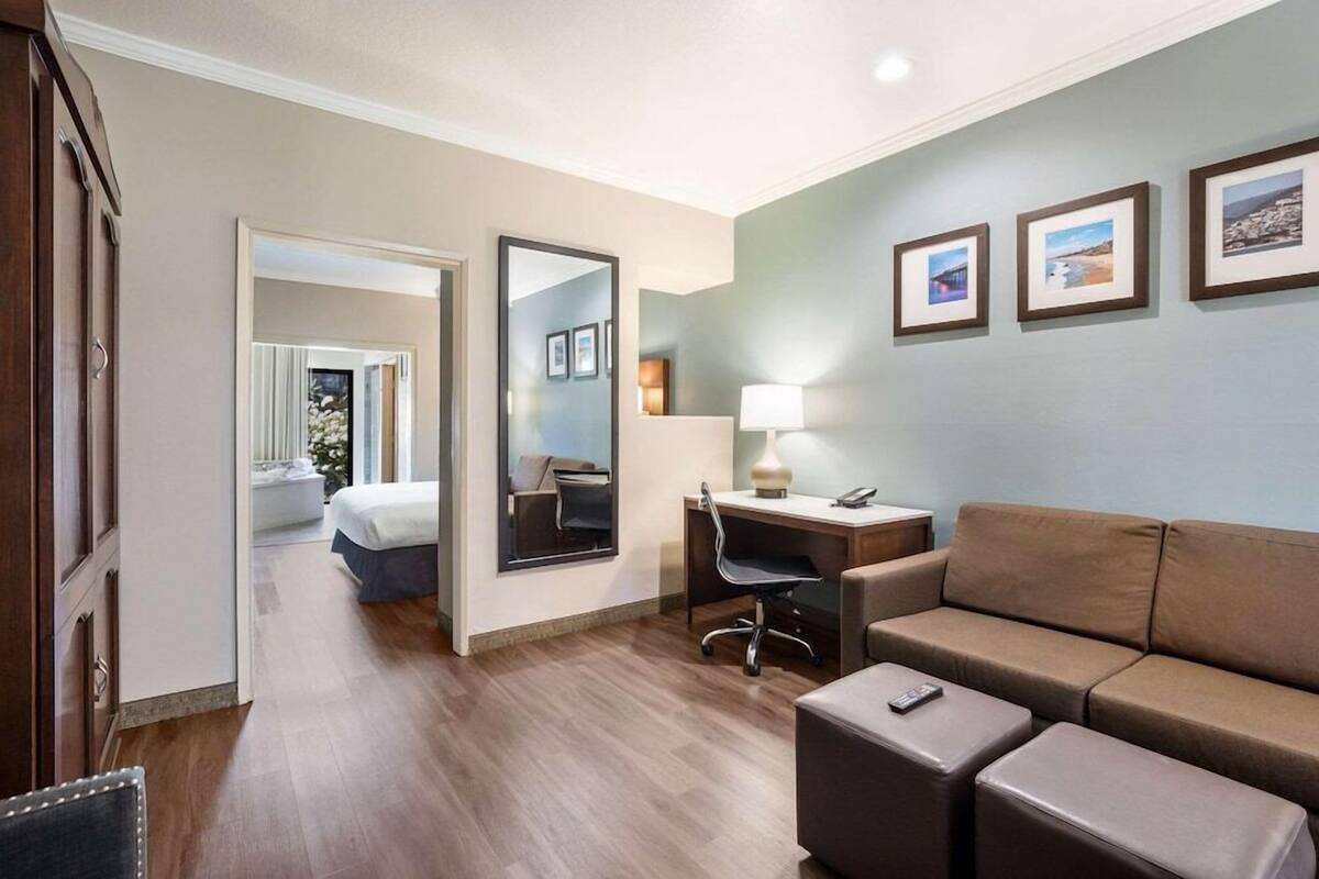 A hotel room with a bed, a desk, a chair, a sofa, a mirror, and framed pictures on the wall.
