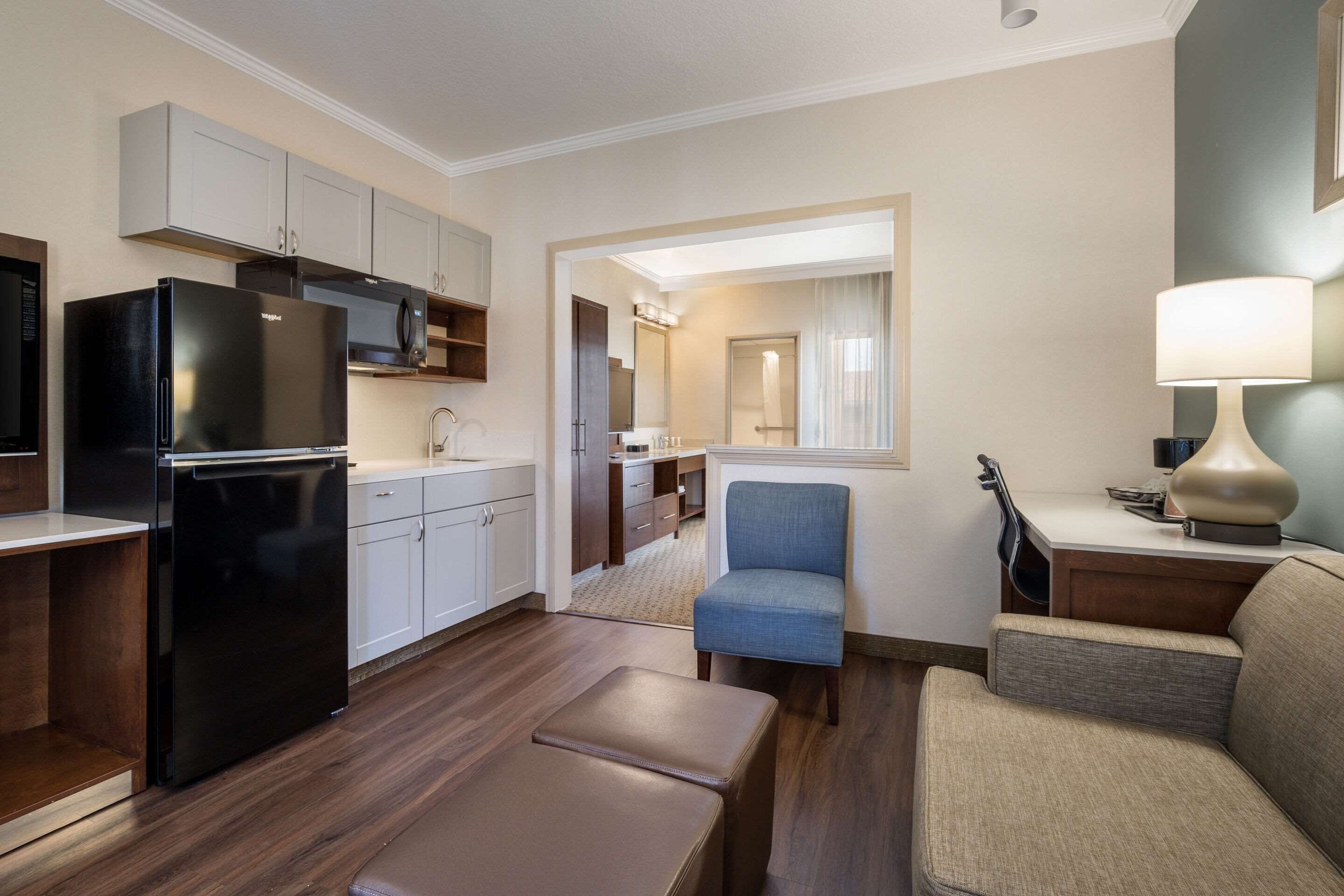 A modern kitchen with white cabinets, a black refrigerator, and a dining area with a blue chair and a beige sofa.