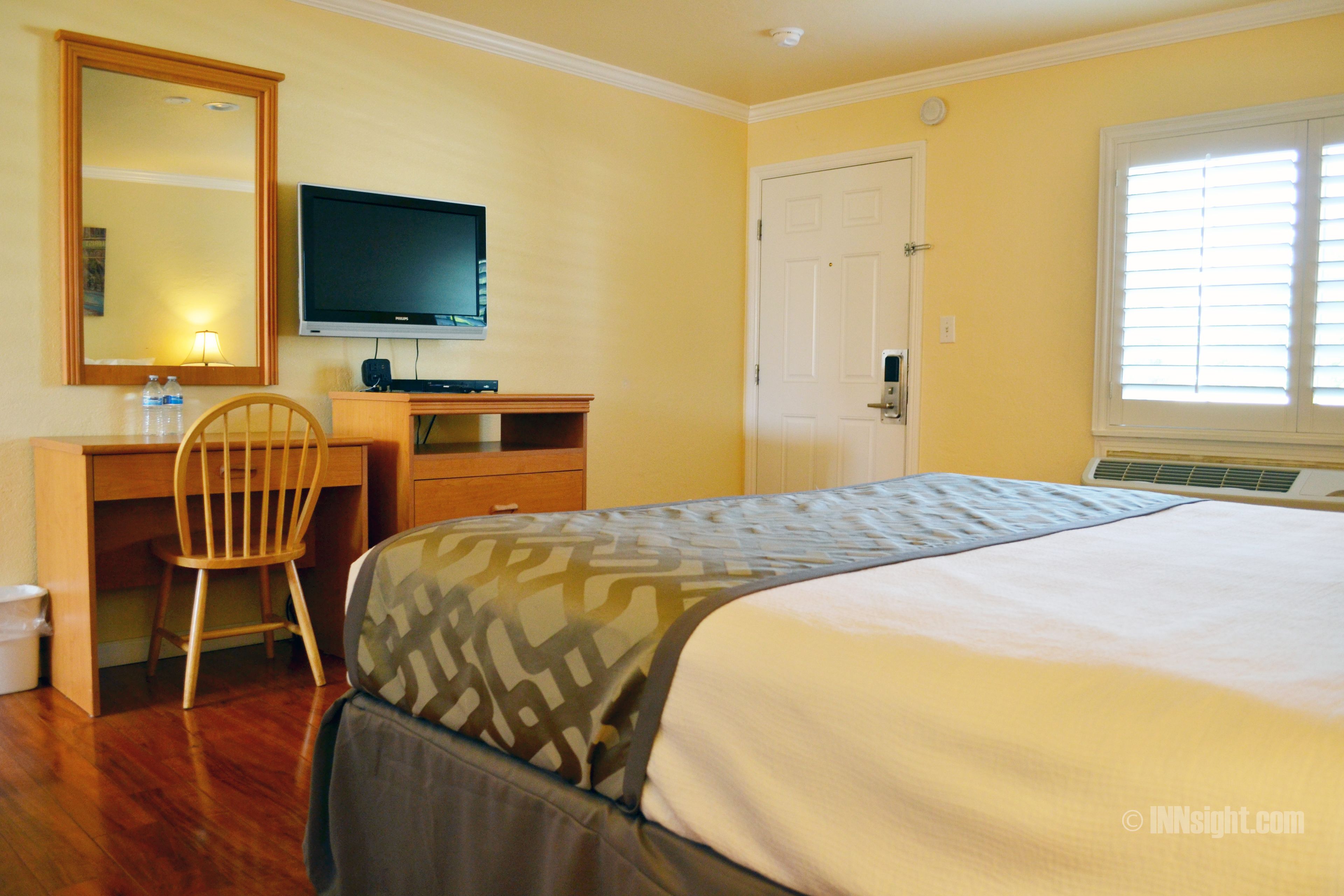 Una habitación de hotel con una cama, un escritorio con computadora, una silla, un televisor y una puerta.