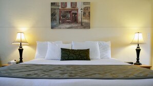 A hotel room with a bed, two bedside lamps, a painting on the wall, and a nightstand with a lamp. - Wittle Inn (Sunnyvale)