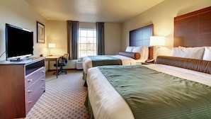 A hotel room with two beds, a desk with a chair, a television, and a window with curtains. - Castle Rock Inn & Suites (Quinter)