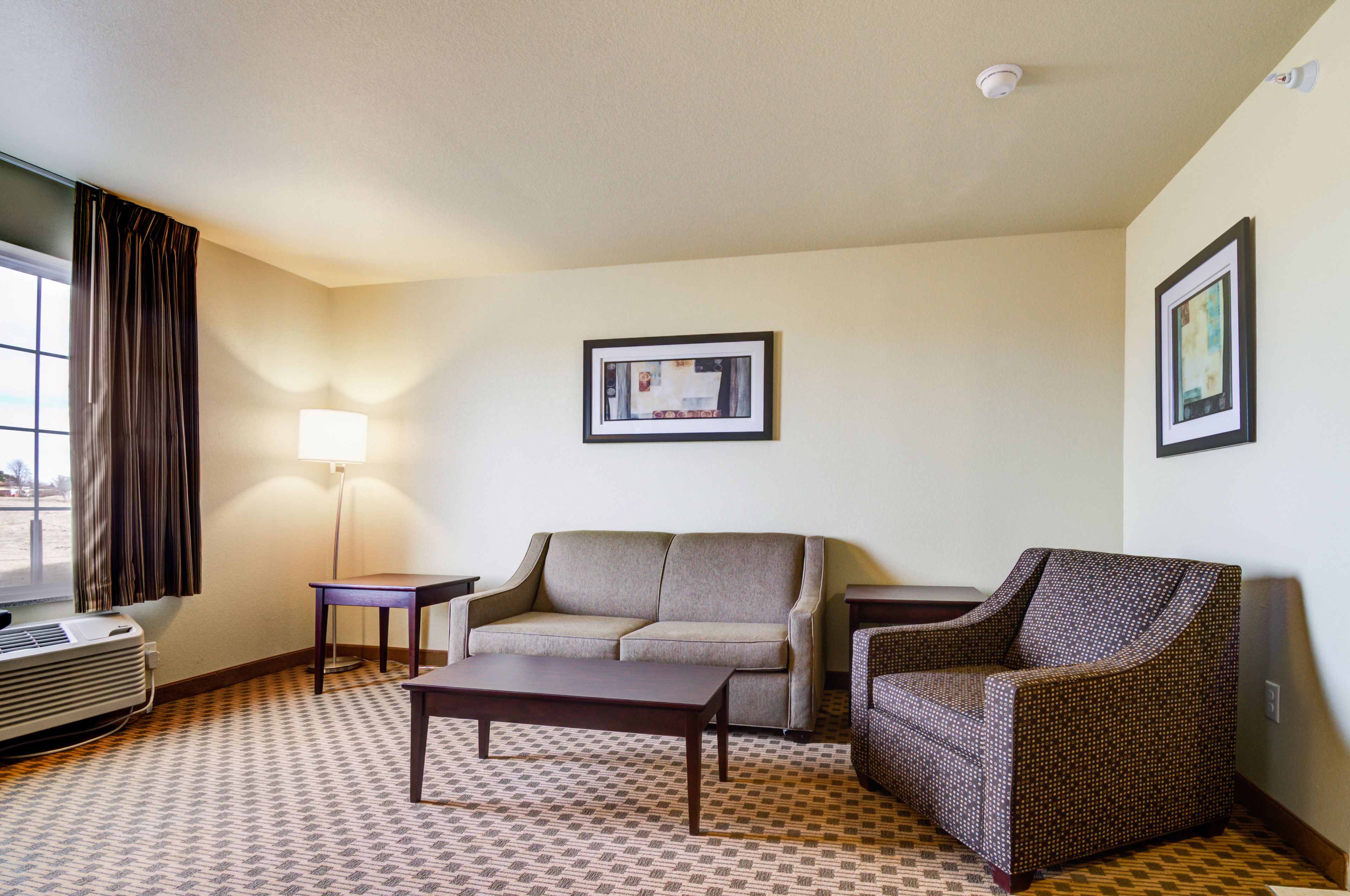Habitación de hotel con sofá, sillón, mesita, lámpara y cuadros en la pared.