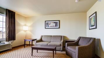 Habitación de hotel con sofá, sillón, mesita, lámpara y cuadros en la pared.