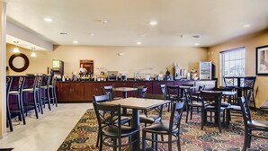 A hotel lobby with a bar area, multiple seating arrangements, and a patterned carpet. - Castle Rock Inn & Suites (Quinter)