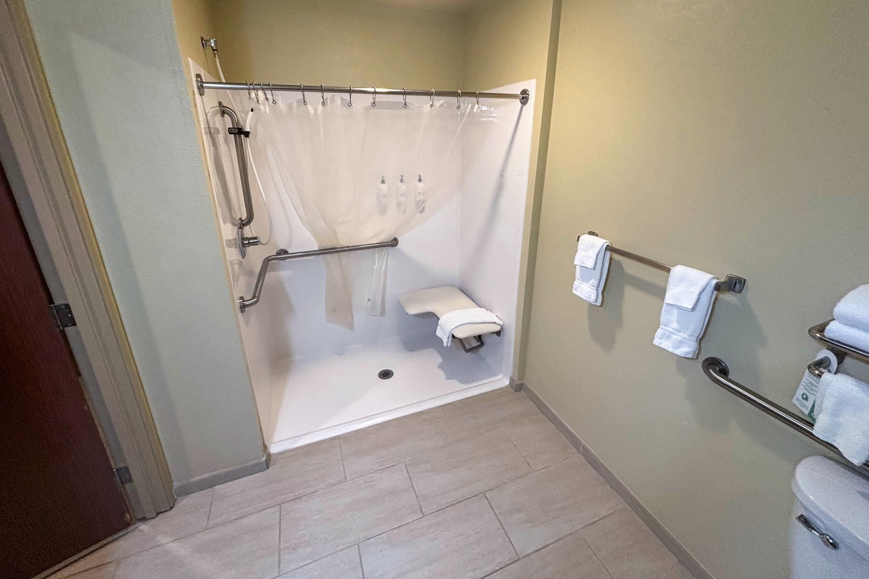 Un baño con ducha, inodoro y barras de apoyo.