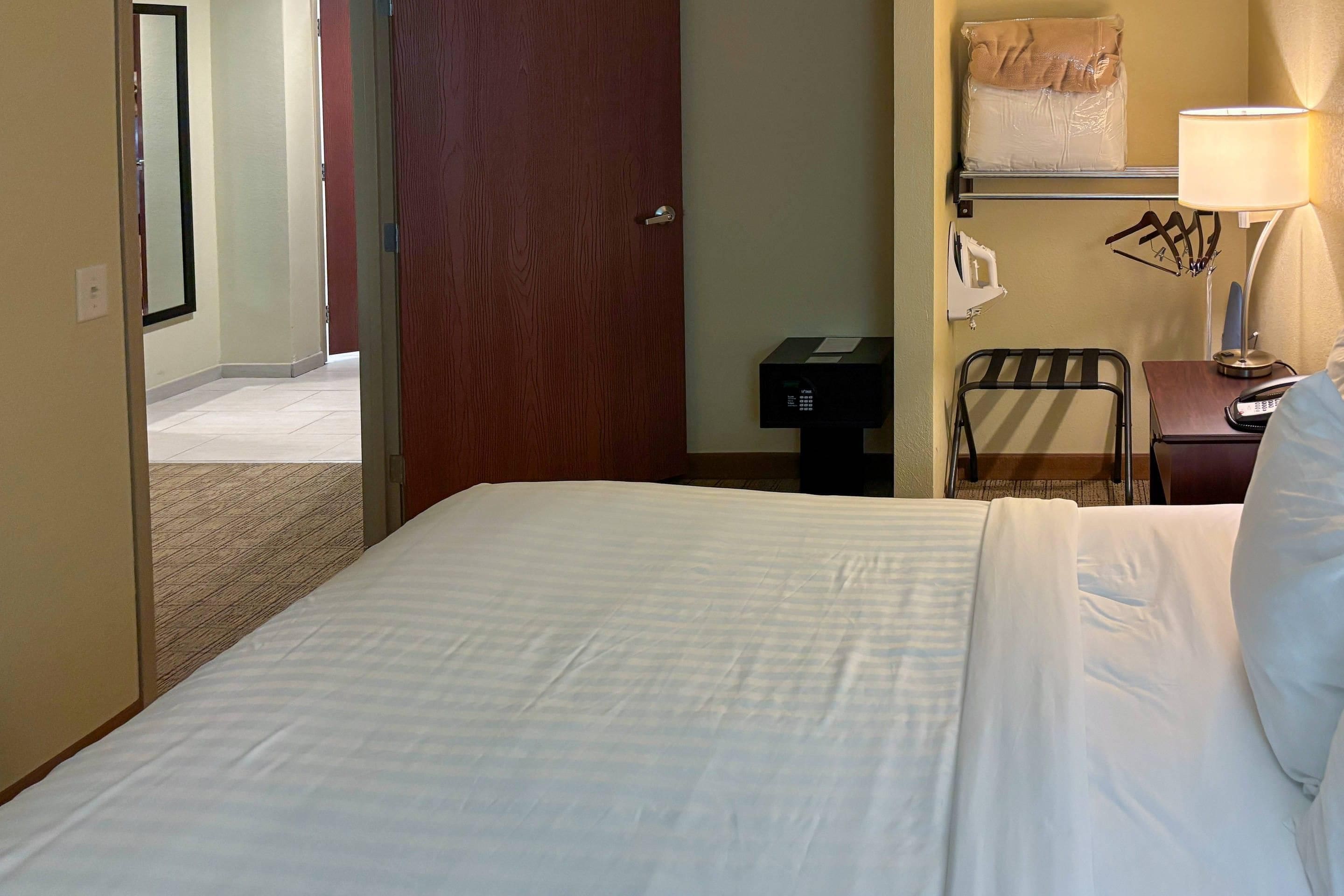 A hotel room with a bed, a desk with a lamp, a chair, and a wall-mounted telephone.