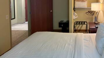 A hotel room with a bed, a desk with a lamp, a chair, and a wall-mounted telephone.