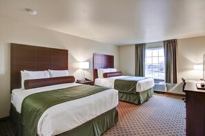 A hotel room with two beds, a desk, a chair, a lamp, and a window with curtains.