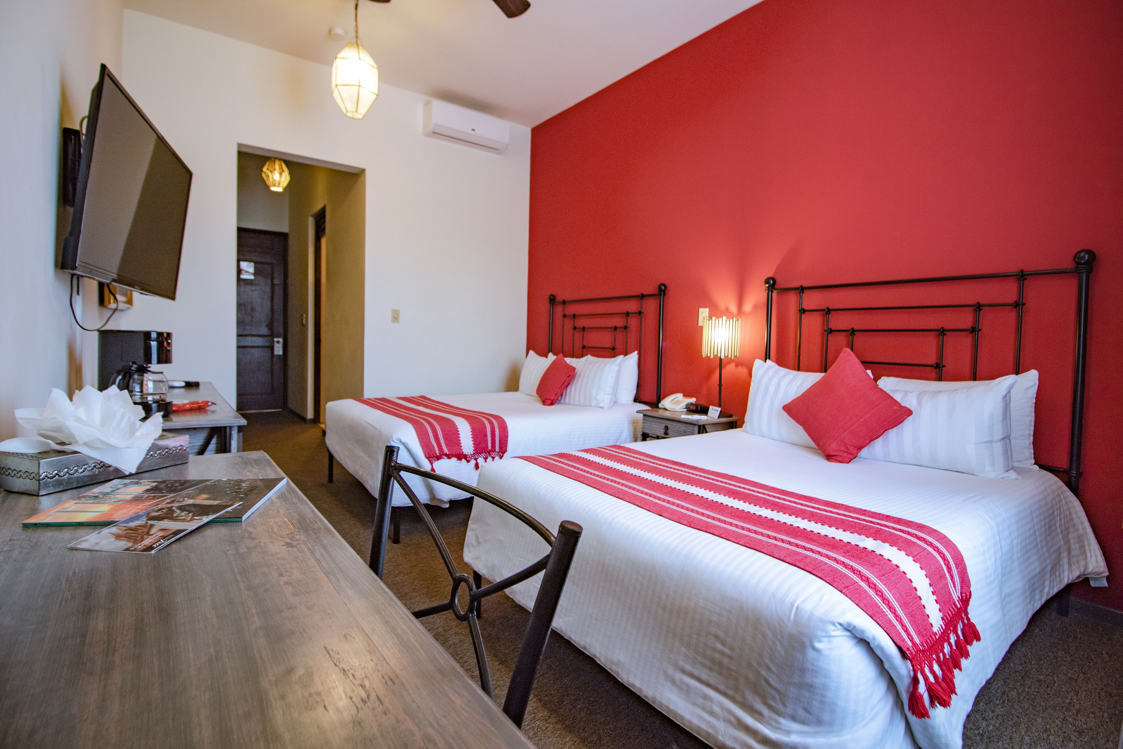 Een hotelkamer met twee bedden, een televisie, een bureau en een rode accentmuur.