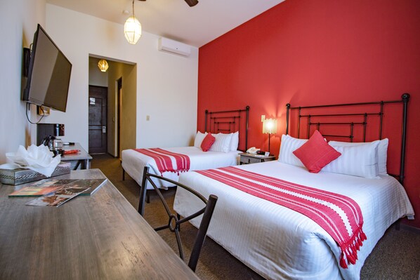 Habitación de hotel con dos camas, televisor, escritorio y una pared de acento roja.