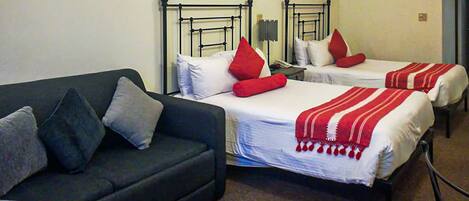 A hotel room with two single beds, a dark-colored sofa, and a radiator.