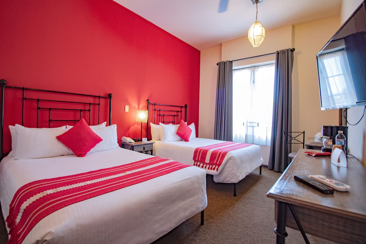 Habitación de hotel con dos camas, un escritorio, un televisor y una ventana con cortinas.