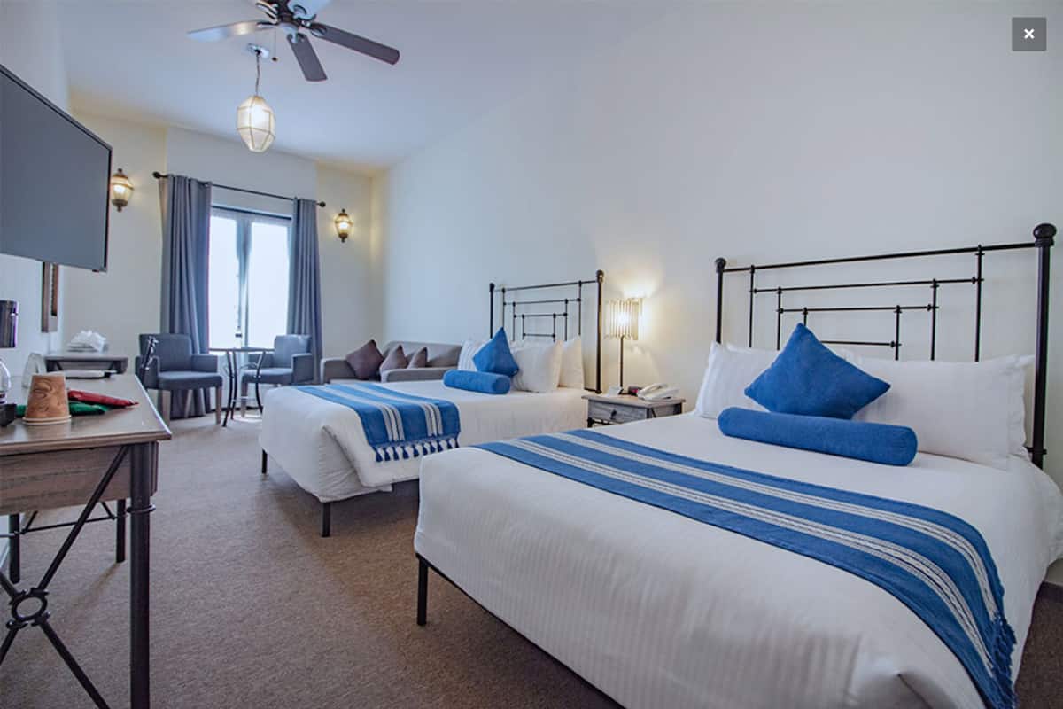 Habitación de hotel con dos camas, un escritorio, una silla, un televisor y una ventana con cortinas.
