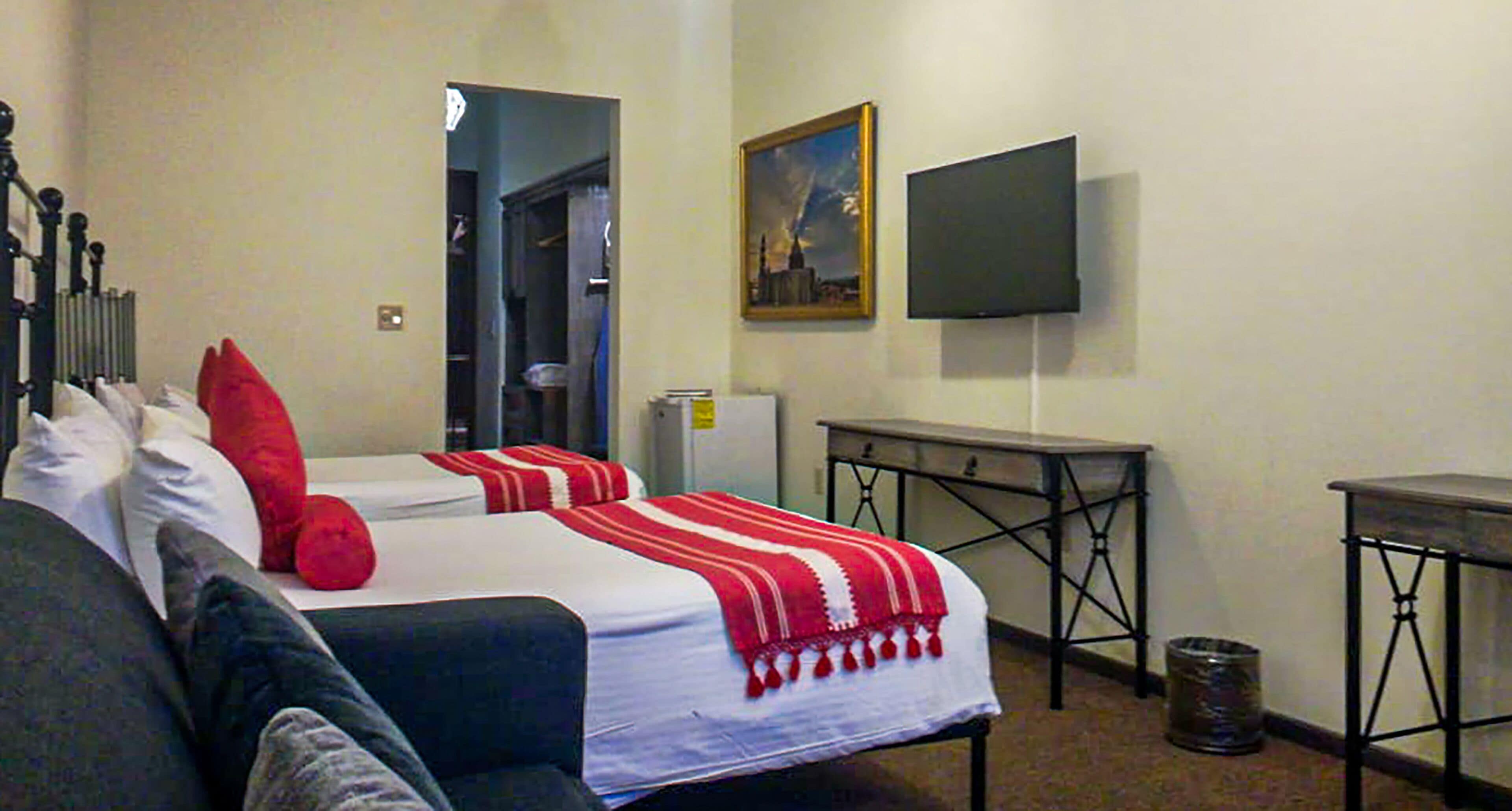 A hotel room with two beds, a TV, a small table, and a trash can.