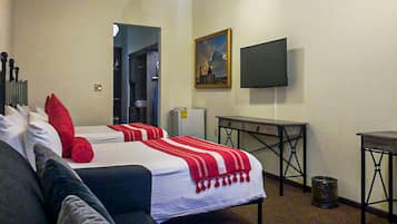 A hotel room with two beds, a TV, a small table, and a trash can.