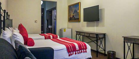 Una habitación de hotel con dos camas, un televisor, una mesita y un cubo de basura.
