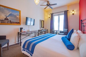 Habitación de hotel con una cama grande, un escritorio con silla, televisión y una ventana con cortinas.