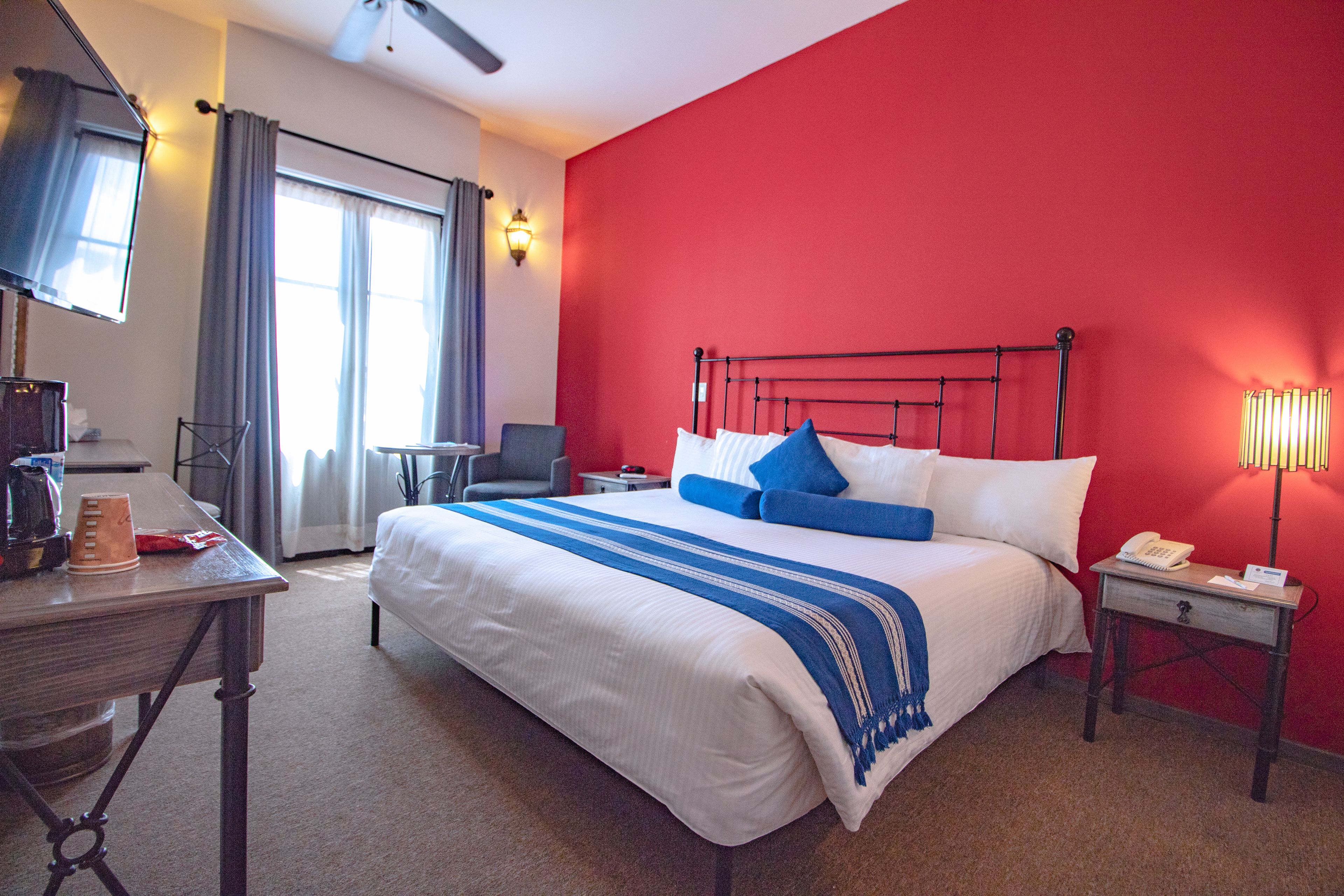 Habitación de hotel con una cama grande, un escritorio con lámpara, una silla y una ventana con cortinas.