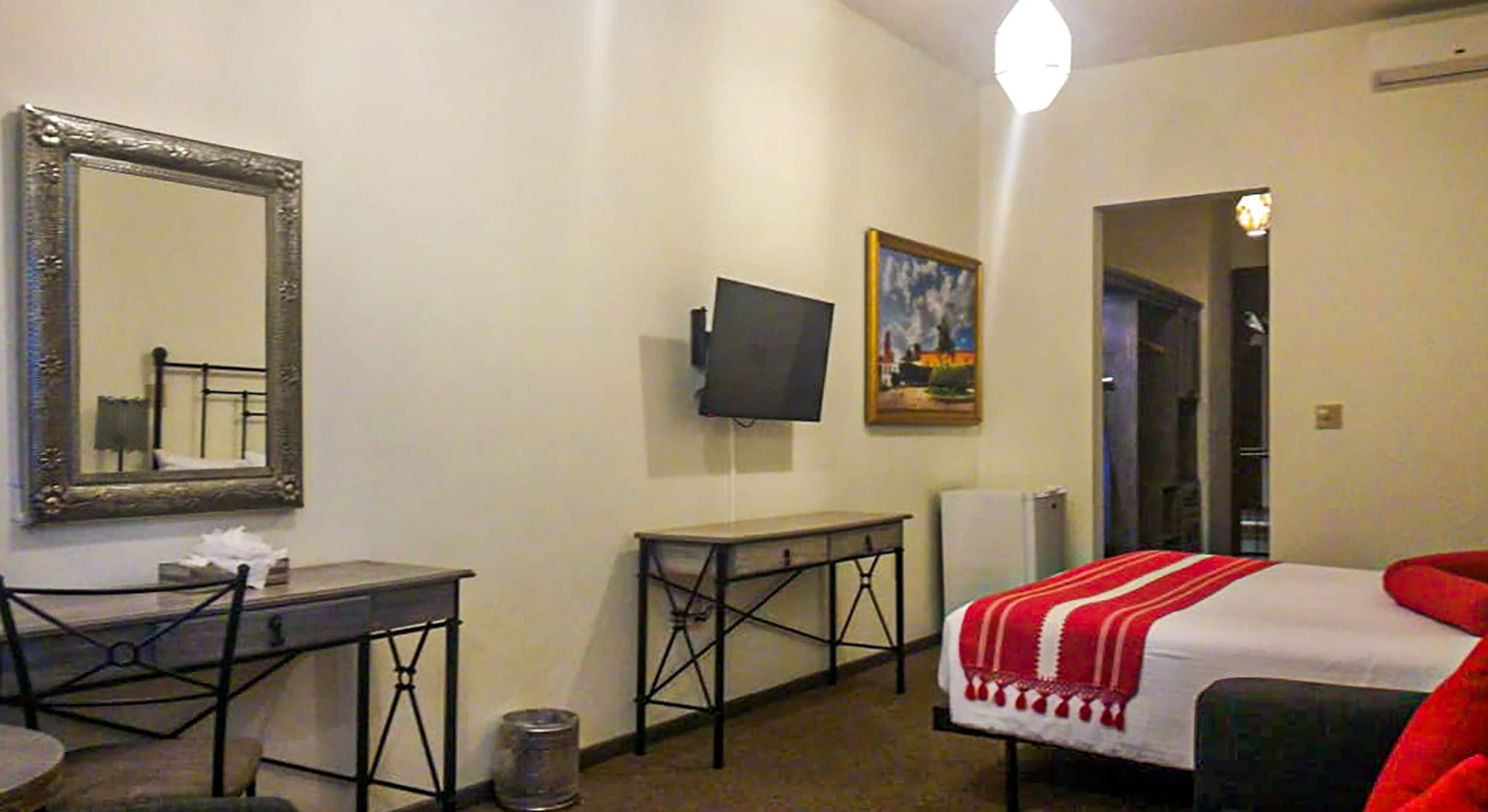 Ein Hotelzimmer mit Bett, Schreibtisch, Stuhl, Fernseher, einem Gemälde und einer Tür zu einem weiteren Raum.