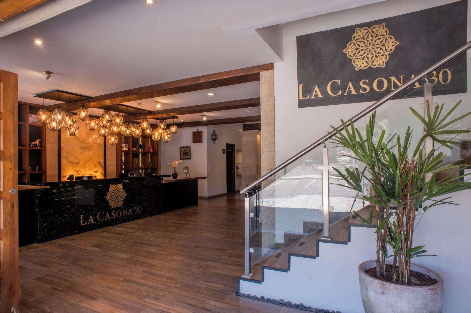 A reception area with a black marble counter, wooden beams, and a staircase with a glass railing.