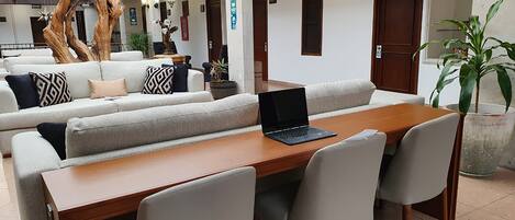 A modern lounge area with a wooden table, white cushioned seating, and a laptop on the table.