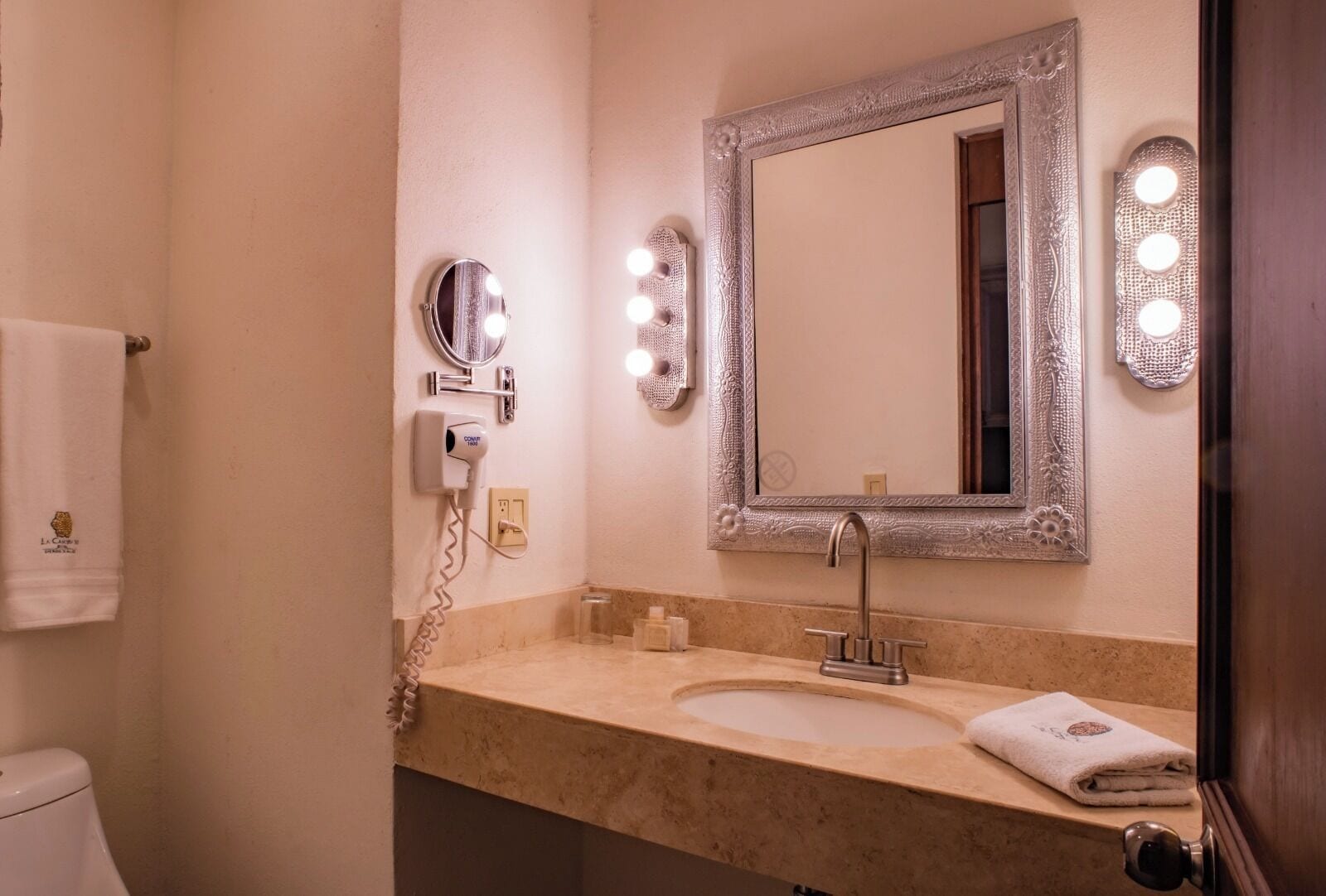 Un baño con tocador, lavabo, espejo con iluminación, secador de pelo y toalla.
